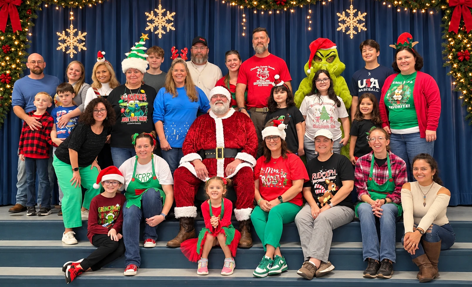 Santa Jeff and the Grinch with a large group in festive outfits beneath glowing snowflakes
